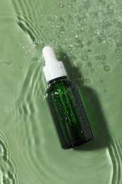 Bottle of cosmetic product in water on pale green background, top view