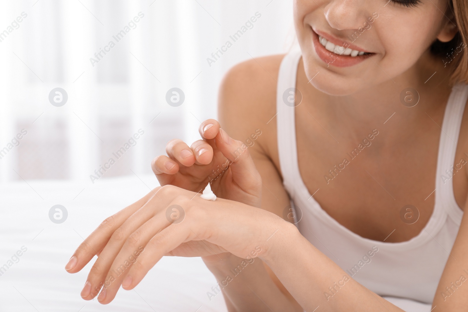 Photo of Young woman applying cream on her hands indoors, closeup. Beauty and body care