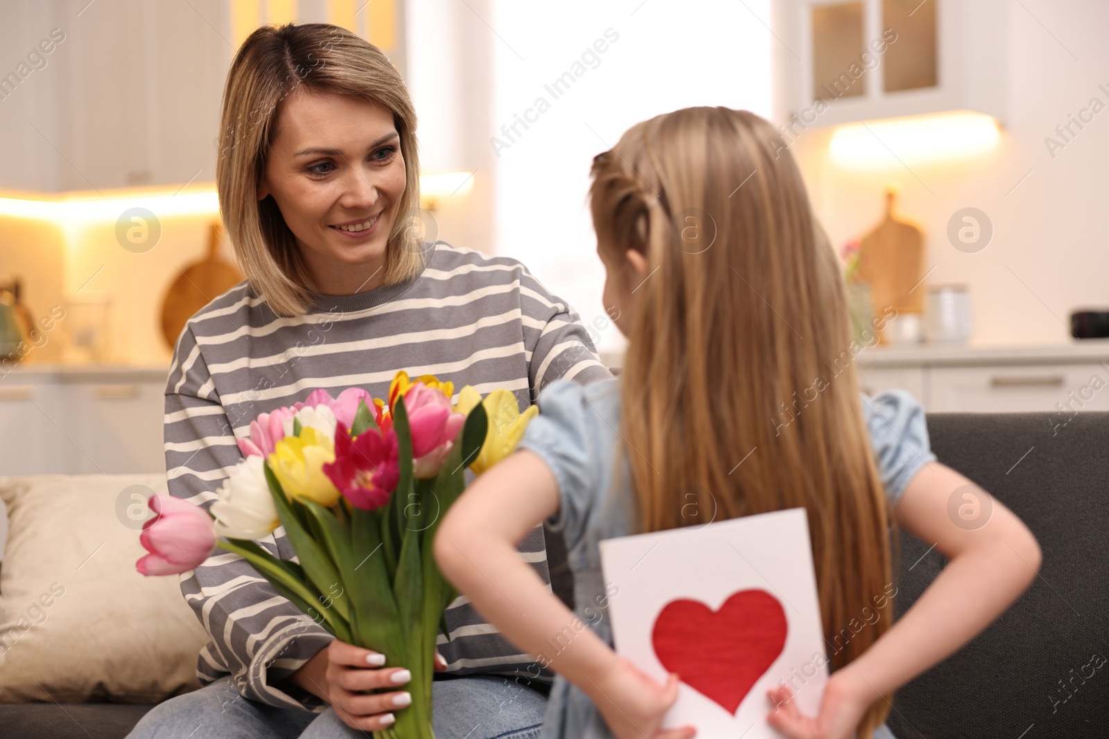 Photo of Little girl hiding greeting card for mom at home, selective focus. Happy Mother's Day