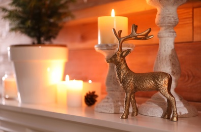 Golden deer figure, candles and decor elements on white mantel indoors