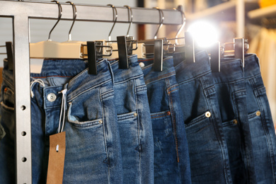 Modern jeans hanging on clothing rack in shop, closeup