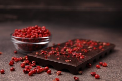 Photo of Delicious chocolate bar and red peppercorns on grey textured table, closeup