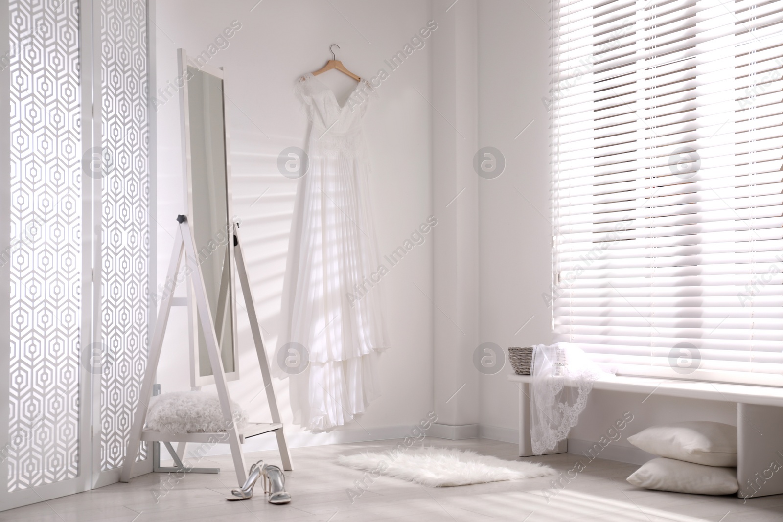 Photo of Beautiful wedding dress hanging on white wall in room