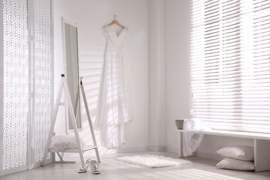 Photo of Beautiful wedding dress hanging on white wall in room