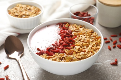 Photo of Smoothie bowl with goji berries and spoon on beige marble table