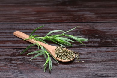 Spoon of dry tarragon and green leaves on wooden table