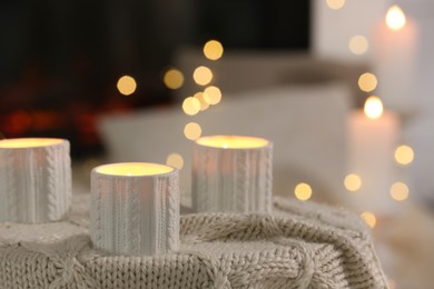 Burning candles on knitted plaid in room. Bokeh effect