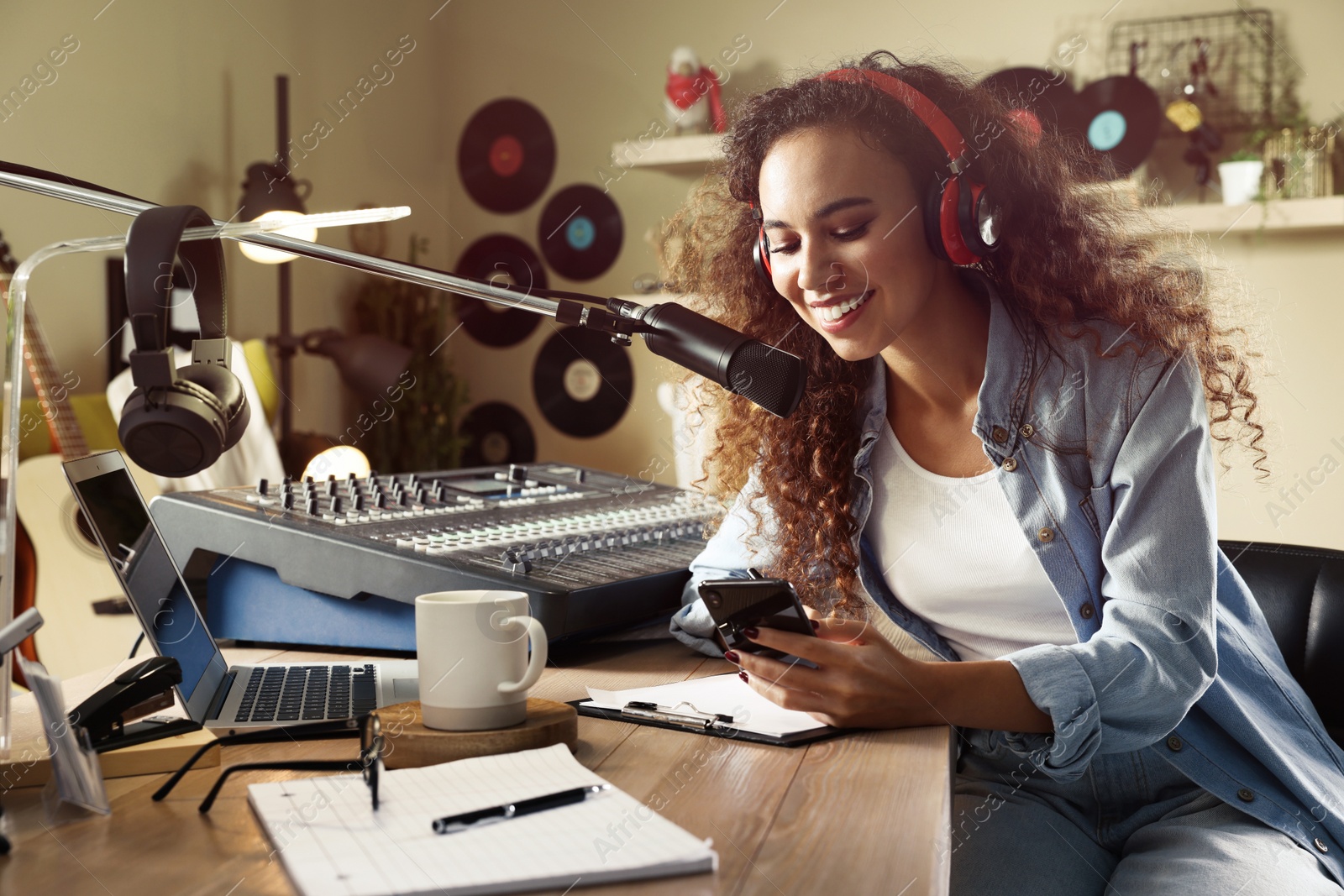 Photo of African American woman with smartphone working as radio host in modern studio