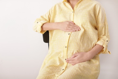 Beautiful pregnant woman sitting on light background, closeup