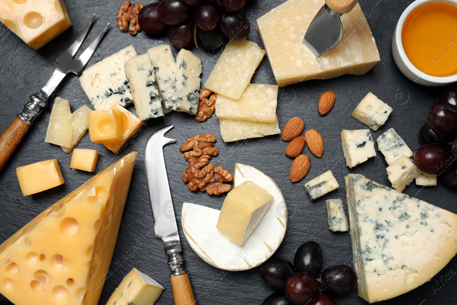 Photo of Cheese platter with specialized knife and fork on black table, flat lay