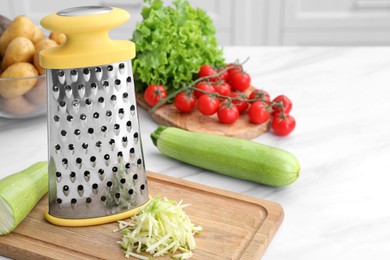 Photo of Grater and fresh vegetables on white table in kitchen. Space for text