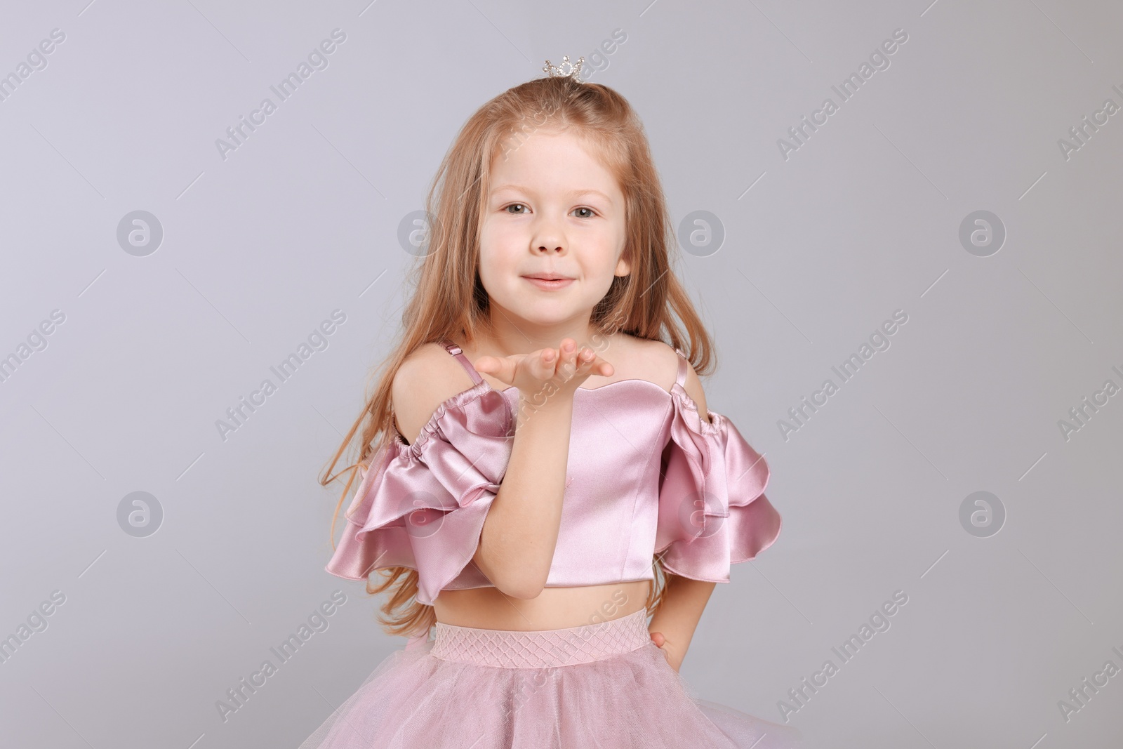 Photo of Cute girl in beautiful dress with small crown on light grey background. Little princess