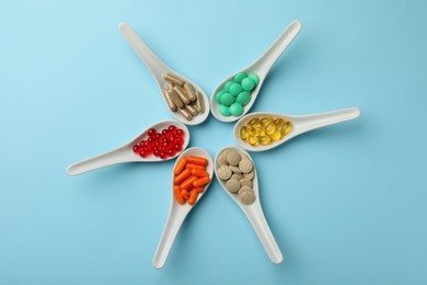 Photo of Spoons with different dietary supplements on light blue background, flat lay