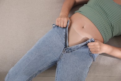 Photo of Woman struggling to squeeze into tight jeans while lying on sofa, closeup