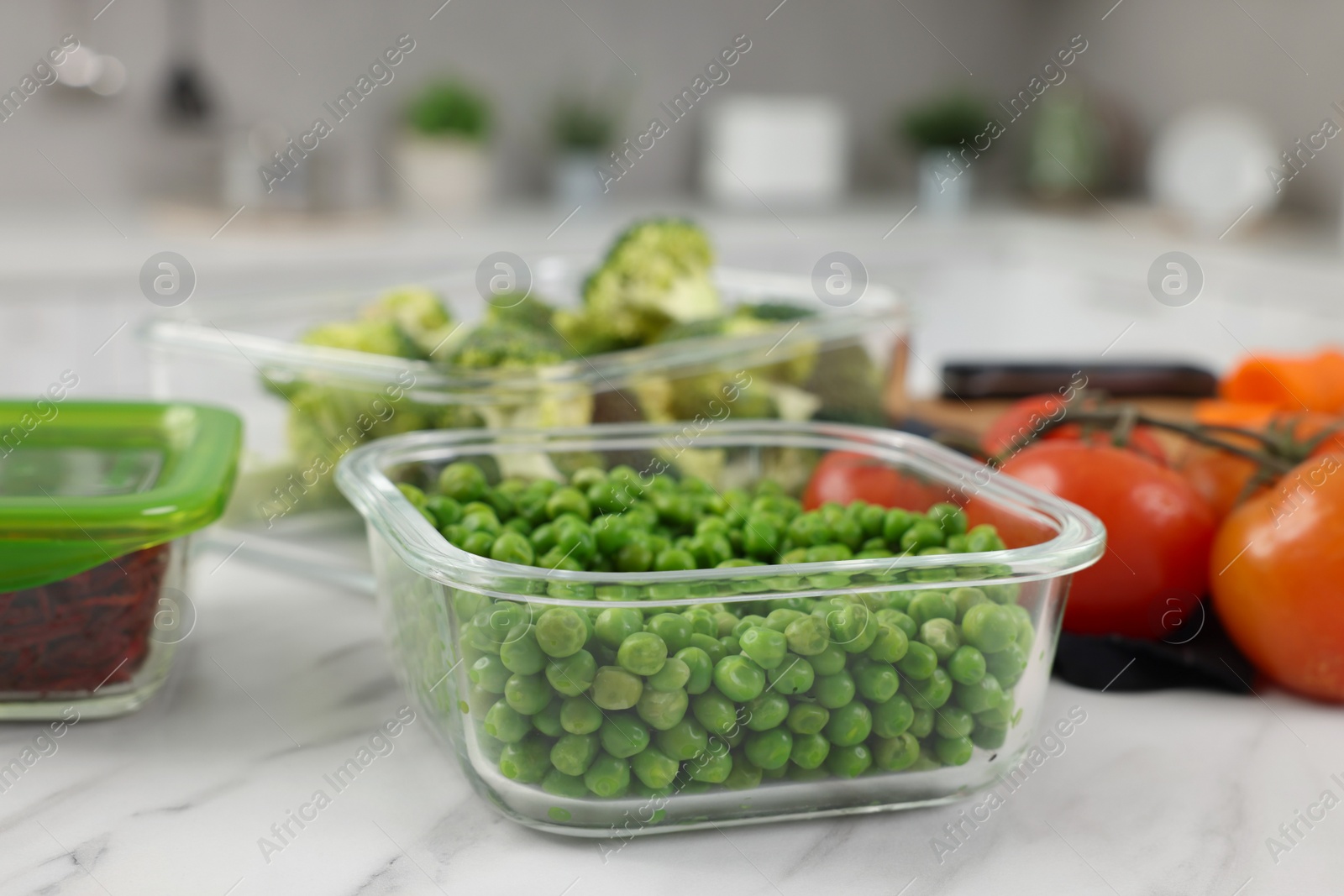 Photo of Container with green peas on white marble table in kitchen, closeup. Food storage