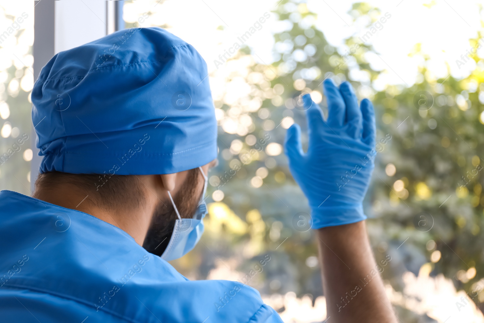 Photo of Stressed doctor near window indoors. Mental pressure of health care workers during COVID-19 pandemic