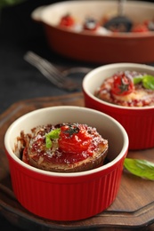 Photo of Baked eggplant with tomatoes, cheese and basil in ramekins on wooden board, closeup