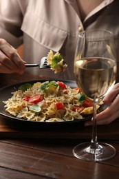 Photo of Woman eating delicious pasta with tomatoes and basil at wooden table, closeup