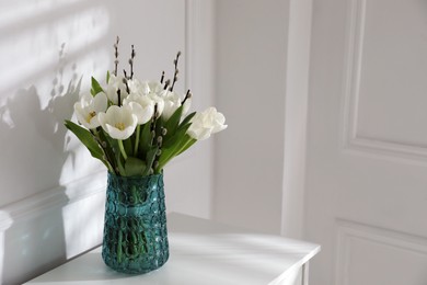 Photo of Beautiful bouquet of willow branches and tulips in vase near white wall indoors, space for text