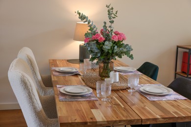 Photo of Beautiful table setting with bouquet indoors. Roses and eucalyptus branches in vase