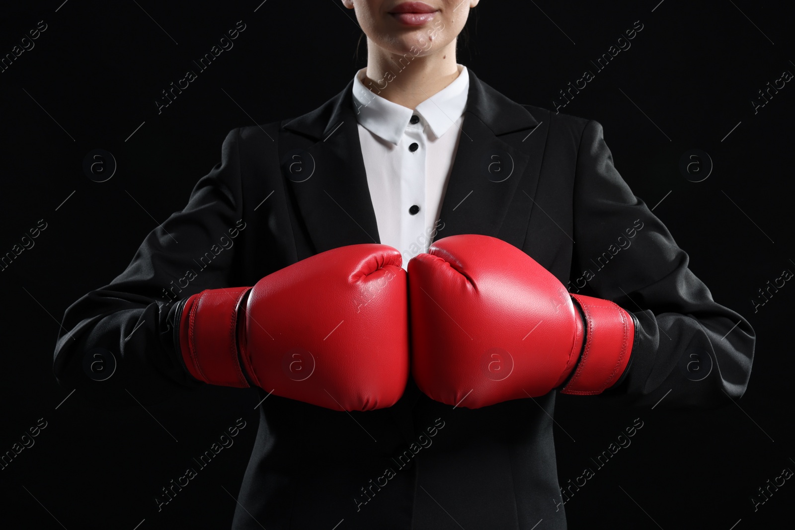 Photo of Businesswoman in suit wearing boxing gloves on black background, closeup