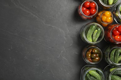 Pickling jars with fresh vegetables on black table, flat lay. Space for text