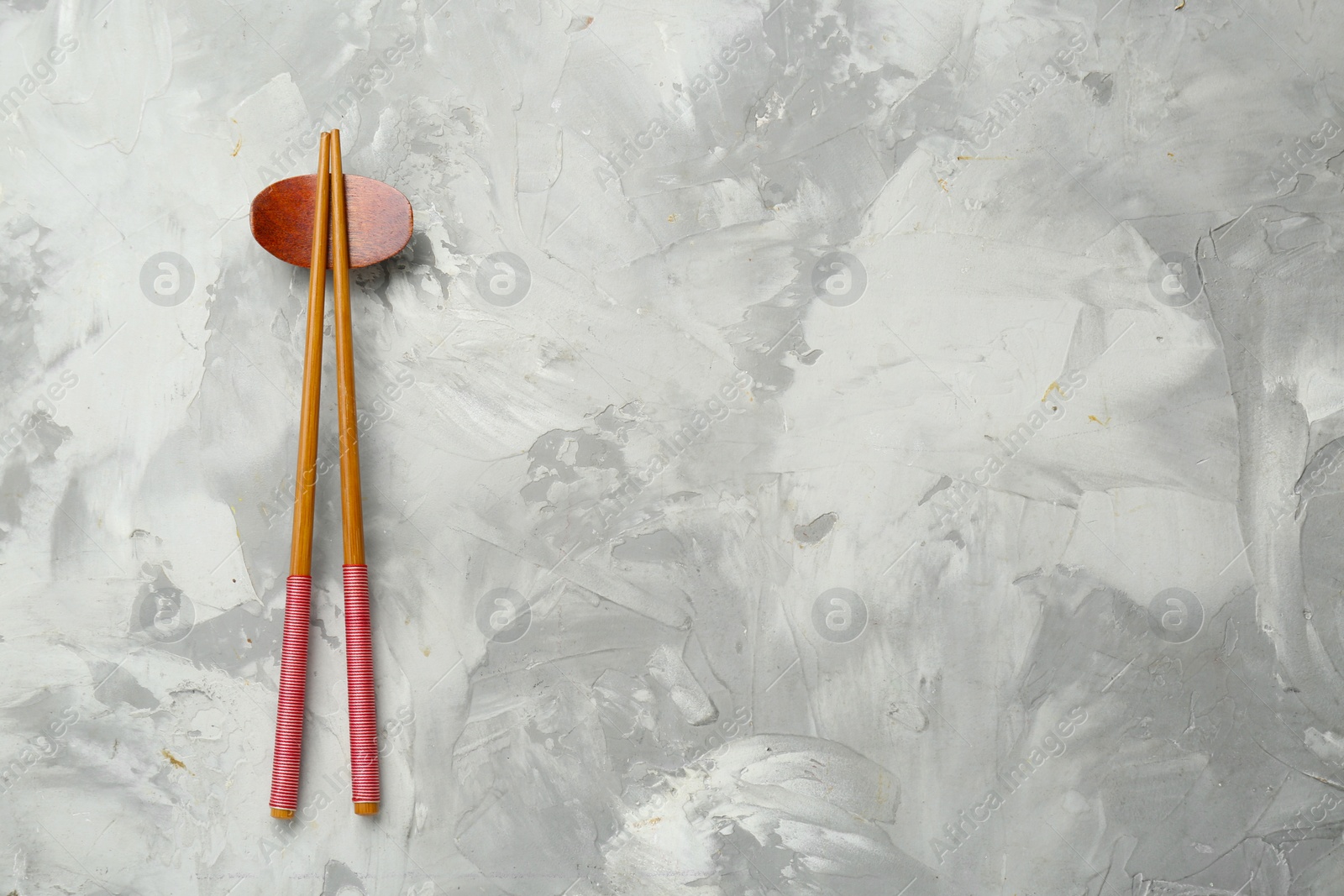 Photo of Pair of wooden chopsticks with rest on grey textured table, top view. Space for text