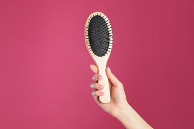 Photo of Woman holding wooden hair brush against crimson background, closeup. Space for text