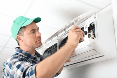 Male technician repairing air conditioner indoors