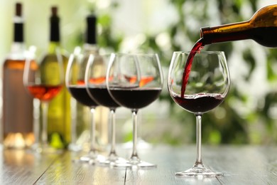 Photo of Pouring red wine from bottle into glass on wooden table