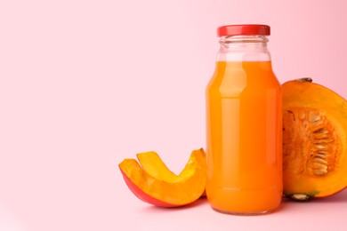 Photo of Tasty pumpkin juice in glass bottle and cut pumpkin on pink background. Space for text