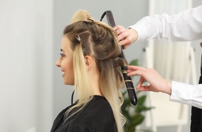 Photo of Hair styling. Hairdresser curling woman's hair in salon, closeup