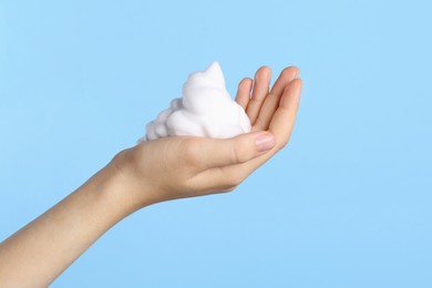 Woman with cleansing foam on light blue background, closeup