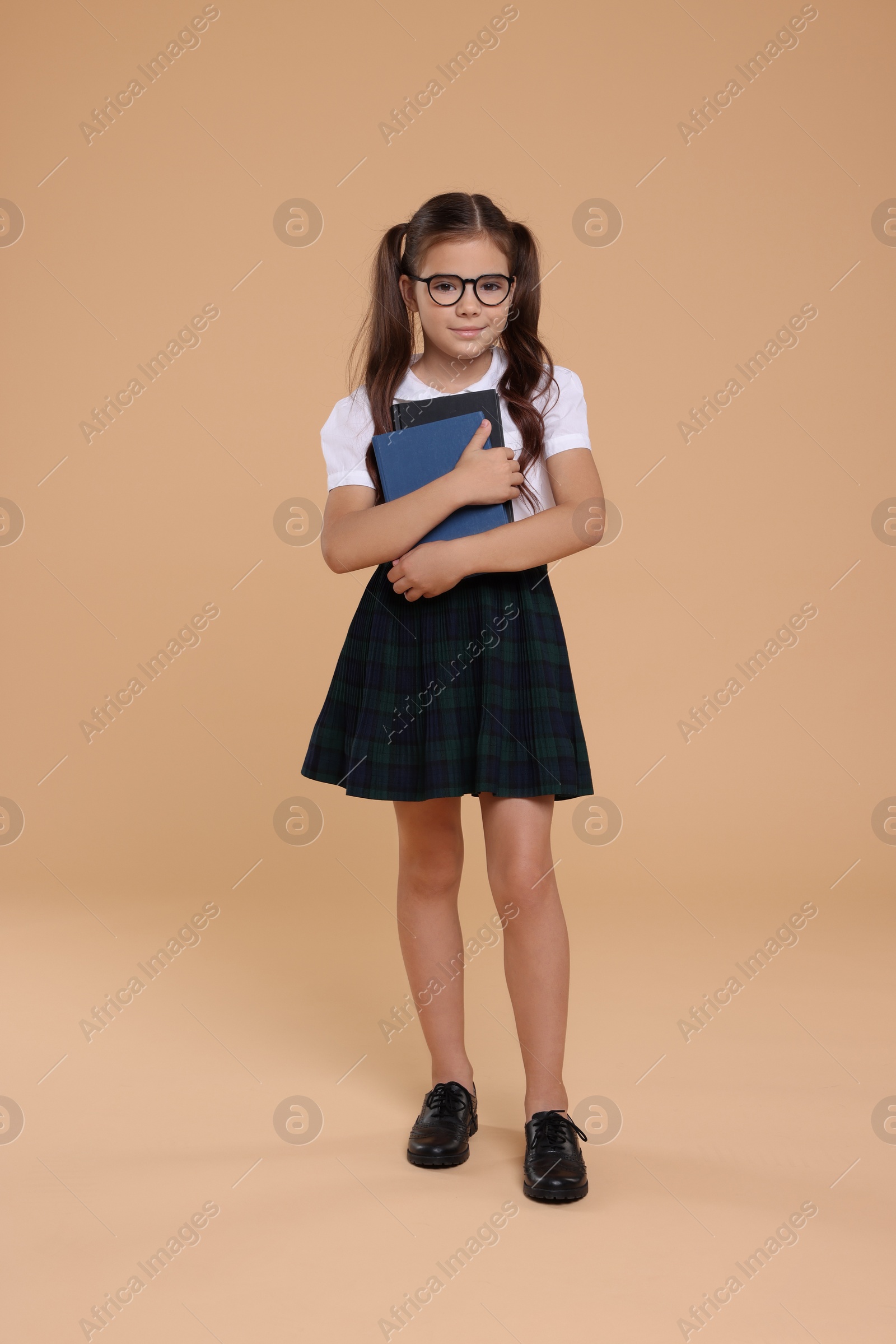 Photo of Cute schoolgirl in glasses with books on beige background