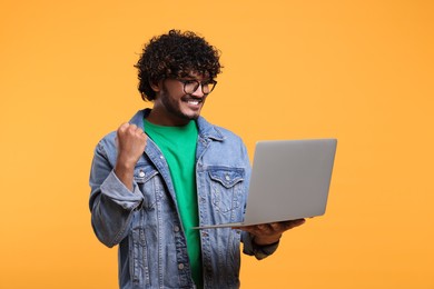 Happy man with laptop on yellow background, space for text