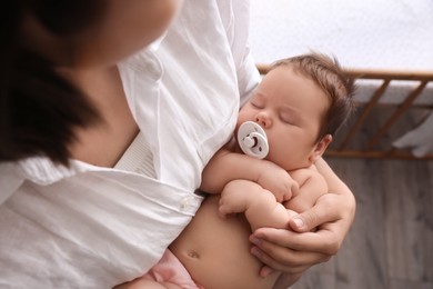 Photo of Mother holding her cute little baby with pacifier at home, above view