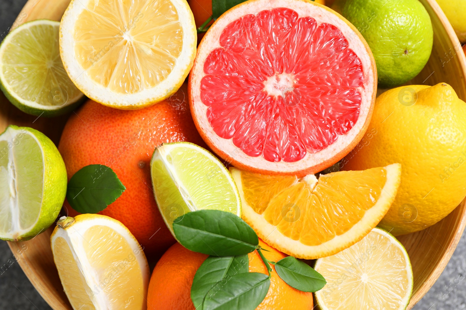 Photo of Different fresh citrus fruits and leaves in bowl on table, top view