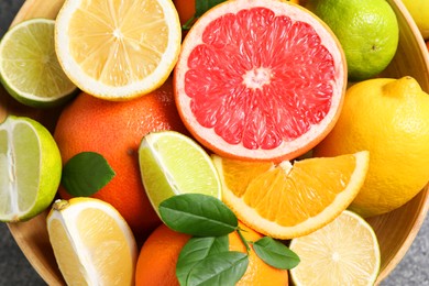 Different fresh citrus fruits and leaves in bowl on table, top view