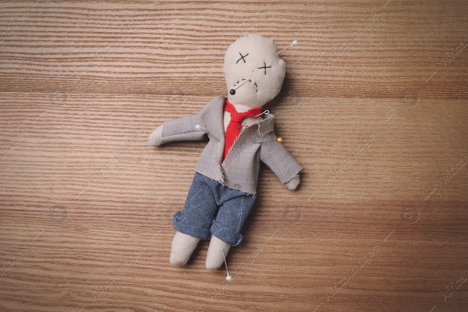 Photo of Voodoo doll pierced with pins on wooden table, top view