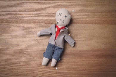 Voodoo doll pierced with pins on wooden table, top view