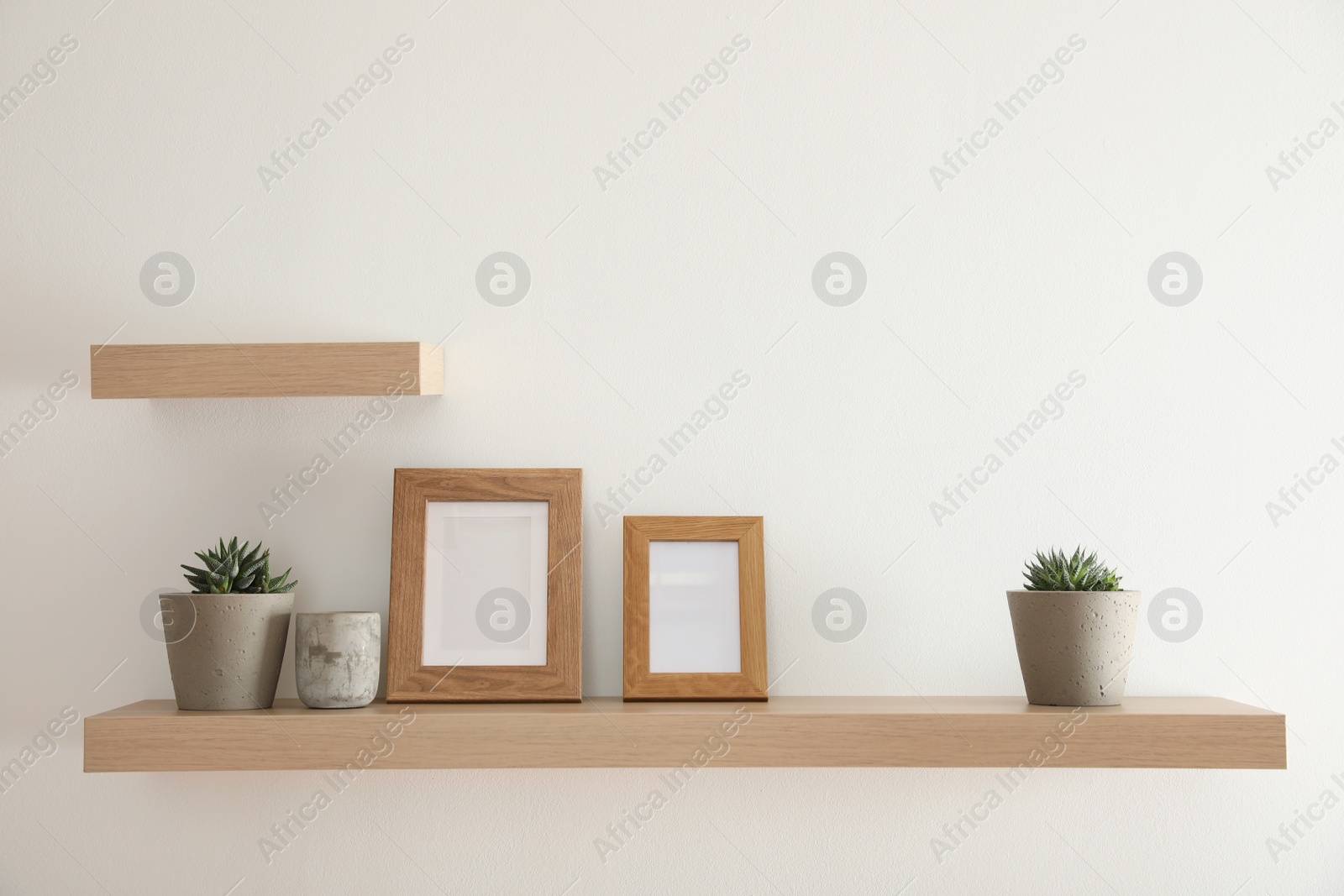 Photo of Wooden shelves with plants and photo frames  on light wall