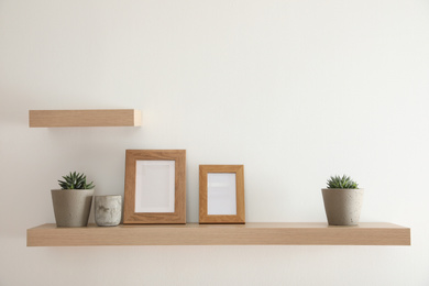 Wooden shelves with plants and photo frames  on light wall