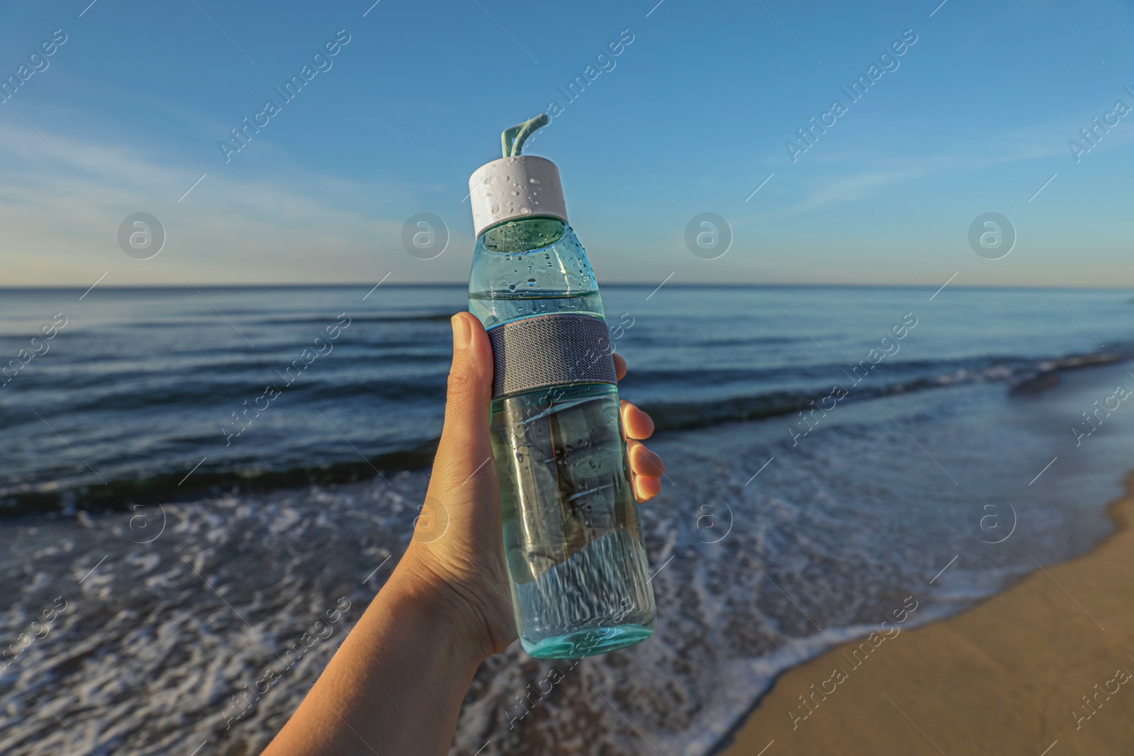 Photo of Woman holding glass bottle with water near sea, closeup