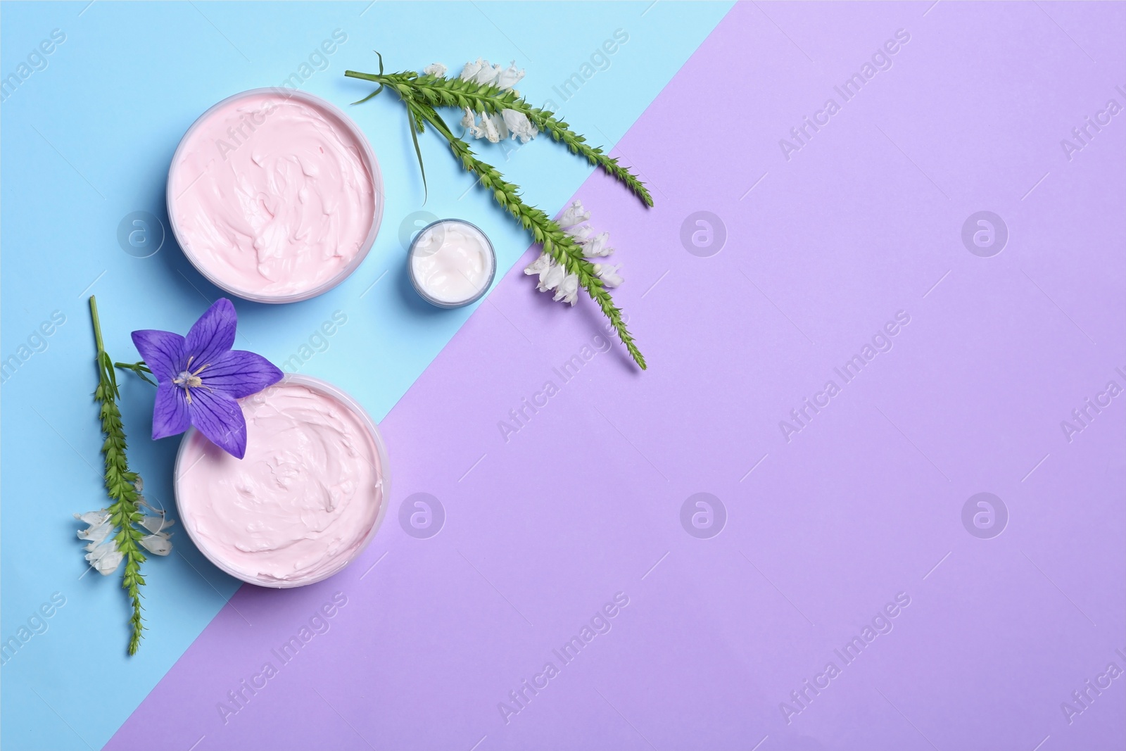 Photo of Flat lay composition with jars of body cream and flowers on color background. Space for text