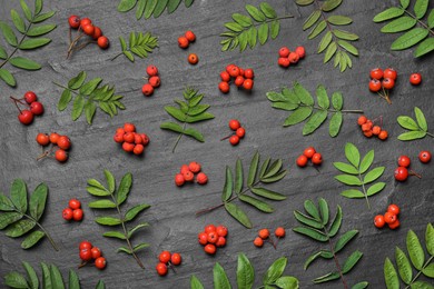 Photo of Fresh ripe rowan berries and green leaves on black table, flat lay