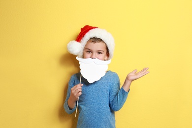 Cute little boy with Santa hat and white beard prop on yellow background. Christmas celebration