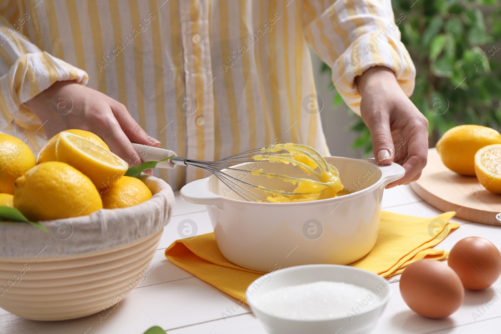 Photo of Woman cooking lemon curd at white wooden table, closeup