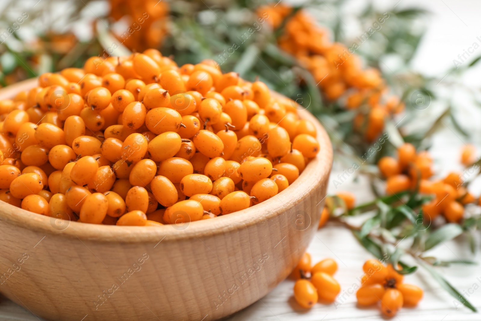 Photo of Fresh ripe sea buckthorn in wooden bowl, closeup