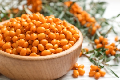 Photo of Fresh ripe sea buckthorn in wooden bowl, closeup