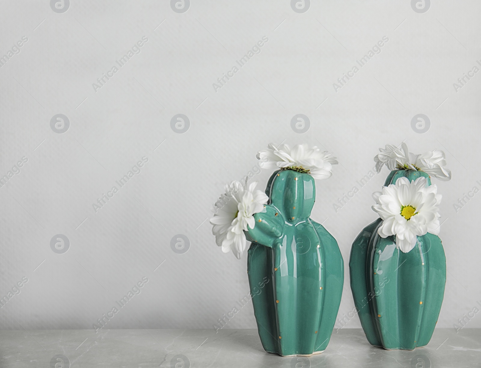 Photo of Trendy cactus shaped vases with flowers on table against light wall. Creative decor